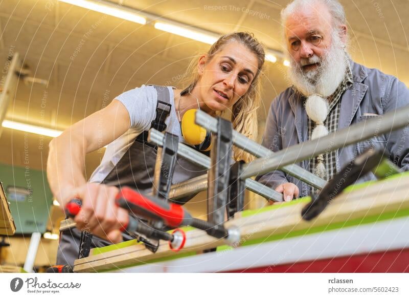 Tischlermeister und Auszubildender verwenden eine Klemme zum Verleimen von Holz in einer Werkstatt professionell Kunsthandwerker Hobelbank Möbelindustrie