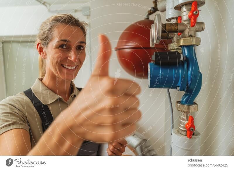 Weiblicher Heizungsbauer zeigt Daumen nach oben in einem Heizungsraum mit einer alten Gasheizung mit Checkliste auf einem Clipboard. Gasheizung Ersatz Verpflichtung Konzept Bild