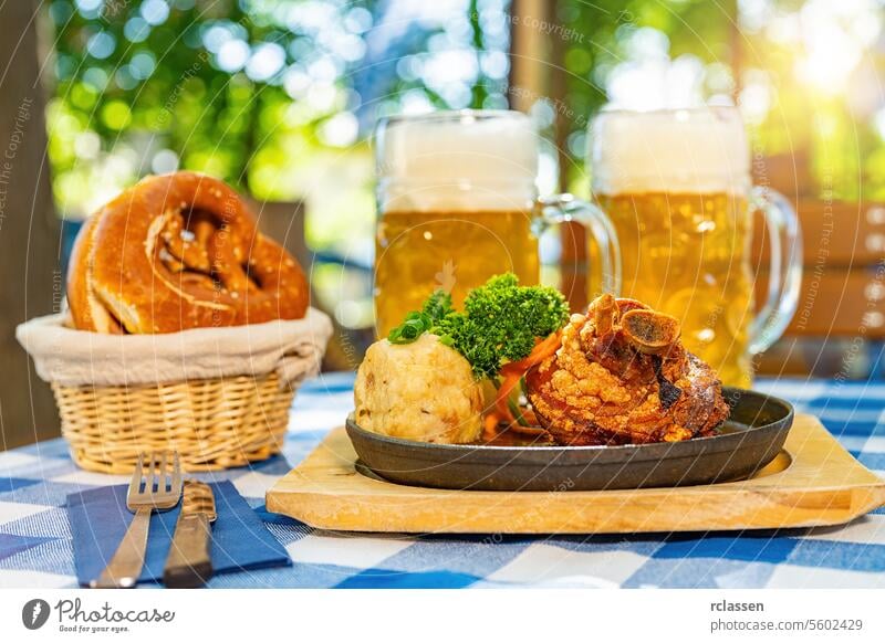 Schweinshaxe, traditionelle bayerische Küche mit gebratener Schweinshaxe mit Kartoffelknödel, Brezen und Bierkrug auf einem Tisch im Biergarten oder auf dem Oktoberfest