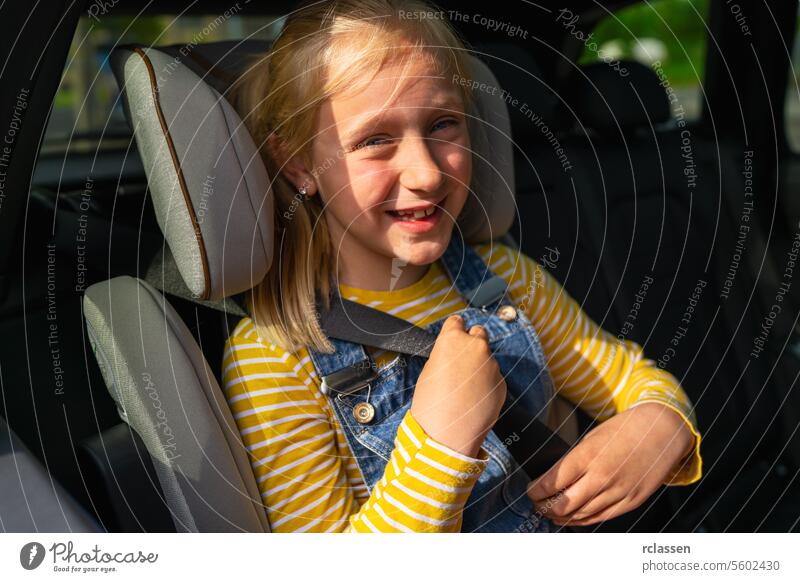 Glückliches Mädchen in Freizeitkleidung schaut in die Kamera und schnallt sich an, während sie auf dem Rücksitz eines Autos während einer Autoreise sitzt