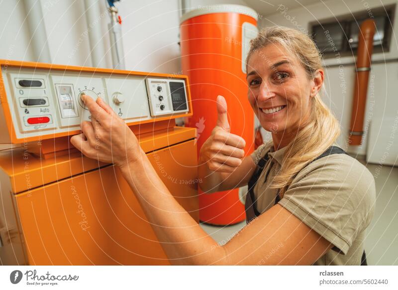 Glückliche weibliche Heizungstechnikerin zeigt Daumen nach oben in einem Heizungsraum mit einer alten Gasheizung mit Checkliste auf einem Clipboard. Gasheizung Ersatz Verpflichtung Konzept Bild