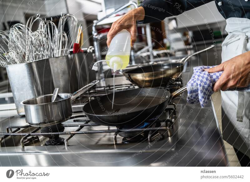 Koch gießt Öl in eine beheizte Pfanne in einem Restaurant. Luxus-Hotel Kochen Konzept Bild. Hand Küche Küchenchef Ölgießen Profiküche Essen zubereiten