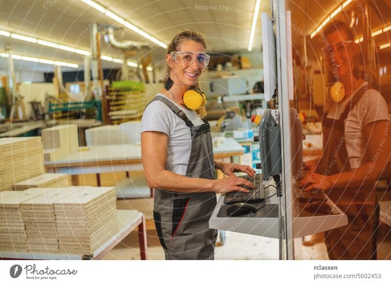 Lächelnde Frau mit Ohrenschützern an einem Computer in einer Schreinerei professioneller Handwerker Möbelindustrie Arbeiter Schnittholz Kapselgehörschützer