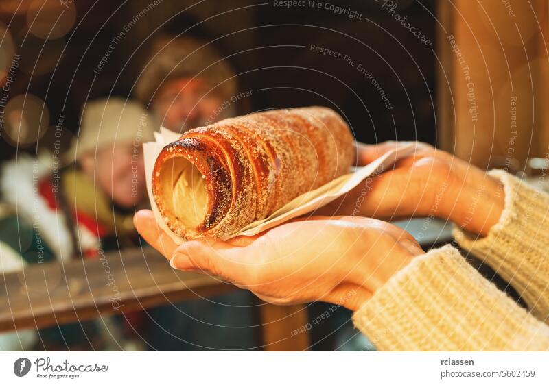 Verkäuferin mit Baumstriezel, Trdelnik oder Kurtoscalacs in der Hand in einer Bude auf dem Weihnachtsmarkt Paar Vollbart alter Mann Dezember Ungarn Brot Laden