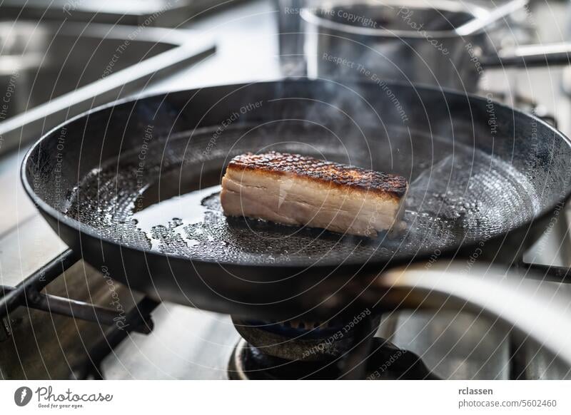 Knuspriger Schweinebauch Braten in heißen Pfanne mit Öl auf einem Gasherd in einer professionellen Küche in einem Restaurant. Luxus-Hotel Kochen Konzept Bild.