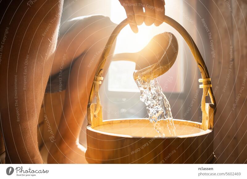Gießen von Wasser aus einem hölzernen Eimer in der finnischen Sauna, Spa und warme Temperatur Bad Therapie Konzept Bild. scroop Nebel platschen Sonnenlicht Hand