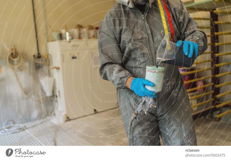 Maler im Schutzanzug gießt blaue Farbe in einen Spritzpistolenbehälter Zimmerer Kunsthandwerker Mundschutz Anstreicher Farbe gießen Container Schutzausrüstung