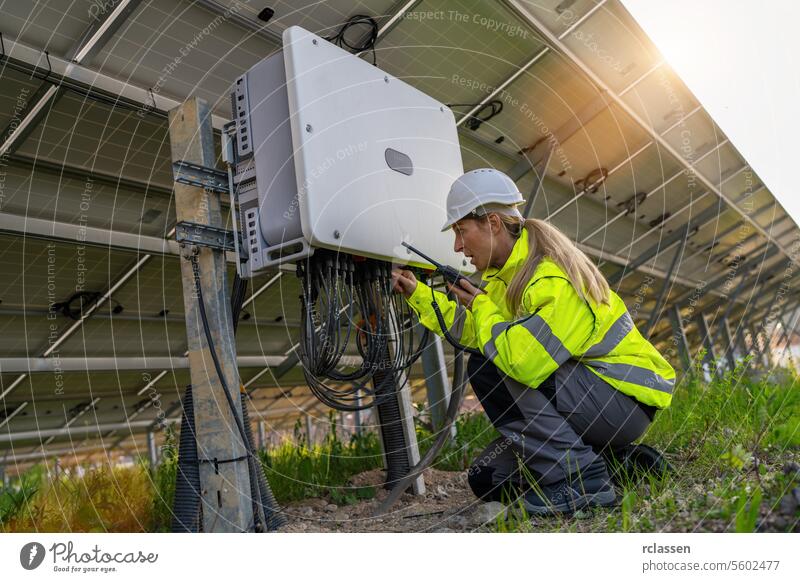 Techniker mit Walkie-Talkie, der einen Verteilerkasten in einem Solarfeld überprüft. Alternative Energie ökologisches Konzept Bild. Meisteringenieur