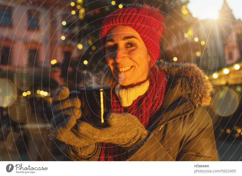 Glückliche Frau vor einem Weihnachtsbaum auf dem Weihnachtsmarkt, die im Winter Glühwein trinkt Verdunstung Dezember Kakao trinken Weihnachten Österreich