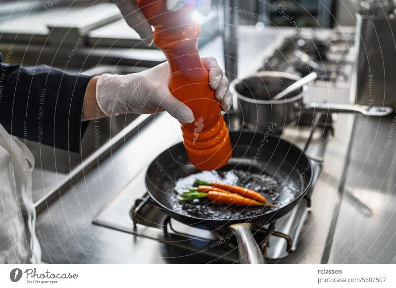 Koch in Hotel oder Restaurant Küche Kochen und Würzen gebratene Karotten in der Pfanne mit einem Pfeffer oder Salzmühle. Luxus Kochen Konzept Bild Mann