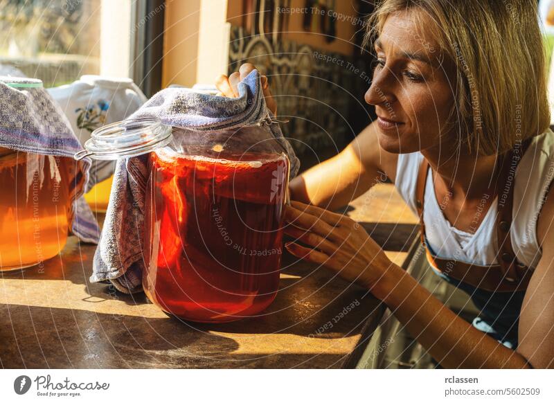 Happy Woman untersucht Kombucha Tee mit Pilz Schichten in einem großen Glas. organische gesunde Getränk fermentierte Lebensmittel, Probiotische Ernährung Getränk für gutes Gleichgewicht Verdauungssystem.