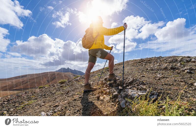 Wanderer in gelber Jacke auf einem Bergpfad vor einem sonnigen, wolkenverhangenen Himmel Fuerteventura gelbe Jacke Sonnenhimmel Wolken Klettern wandern
