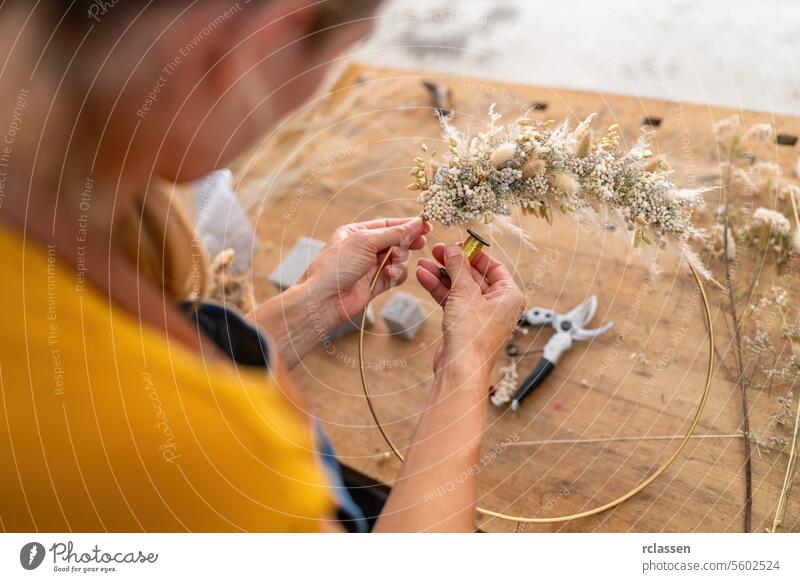 Nahaufnahme der Hände eines Floristen, der getrocknete Blumen auf einen Reifen vor einem Holztisch verdrahtet Blumenhändler Trockenblumen Verkabelung Basteln