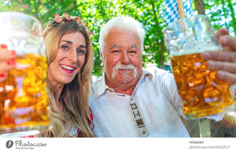Alter Mann und junges Mädchen schauen in die Kamera und sagen Prost oder stoßen mit einem Krug Bier im bayerischen Biergarten oder auf dem Oktoberfest an