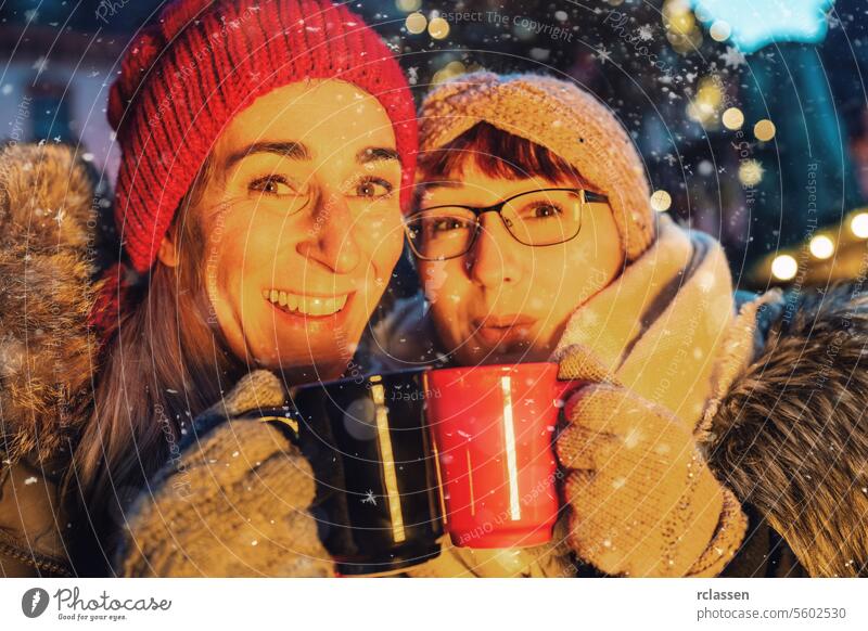 Freunde trinken heißen Glühwein oder Punsch auf einem Weihnachtsmarkt Bowle Frohe Weihnachten Tasse Kakao Handschuhe traditionell Deutsch Schneeflocken Feiertag