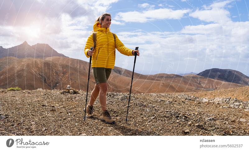 Wanderer in gelber Jacke mit Trekkingstöcken auf einem Bergpfad unter einem bewölkten Himmel Fuerteventura gelbe Jacke Bergweg bewölkter Himmel Abenteuer
