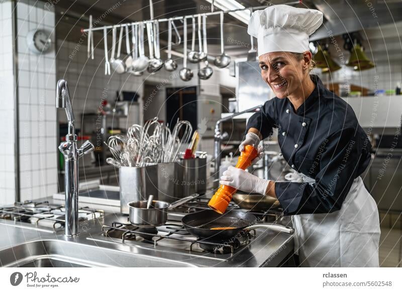 Lächelnde Köchin in Hotel- oder Restaurantküche beim Kochen und Würzen der Speisen mit einer Pfeffer- oder Salzmühle Pfeffermühle Gewürz Uniform Schleifmaschine