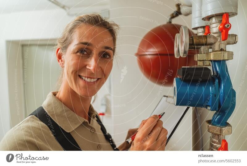 Lächelnder weiblicher Heizungsbauer in einem Gaskesselraum für Heizungsanlagen mit Checkliste auf einem Clipboard. Gasheizung Ersatz Verpflichtung Konzept Bild