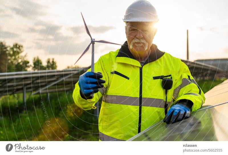 Ein leitender Ingenieur hält ein Windturbinenmodell an einer Photovoltaikanlage bei Sonnenuntergang. Alternative Energie ökologisches Konzept.