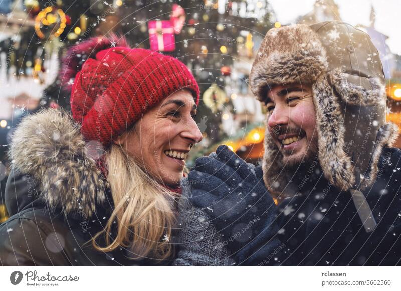 Ein Paar hält sich an den Händen, während im Hintergrund ein festlicher Weihnachtsmarkt zu sehen ist. Freunde Glühwein Vollbart Tourismus Datierung Fairness