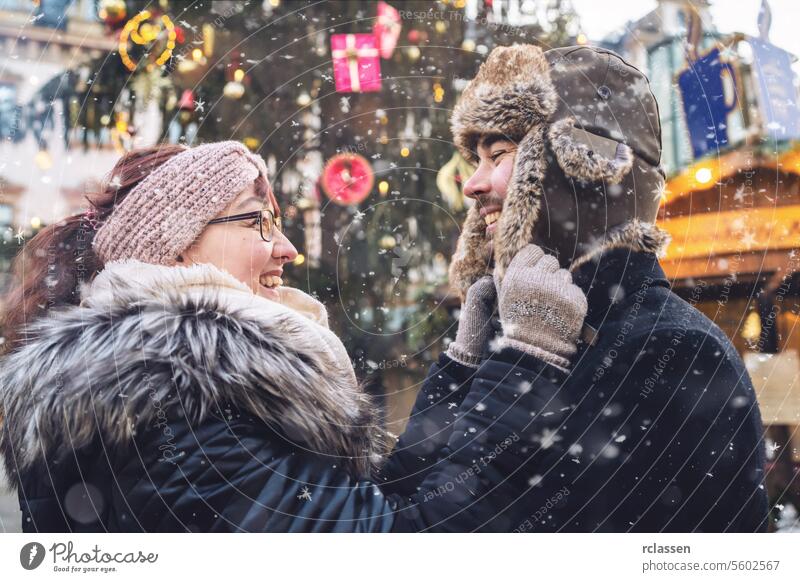 Paar in Winterkleidung lächelt einander an, an einem verschneiten Wintertag auf einem Weihnachtsmarkt Freunde Glühwein Vollbart Tourismus Datierung Fairness