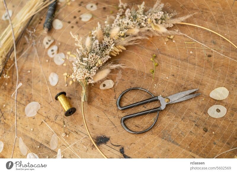 Getrocknetes Blumenarrangement und Schere auf einem Holztisch mit verstreuten Blütenblättern und Fadenspule Werkstatt Mondviole Trockenblumen Gesteck Garnrolle