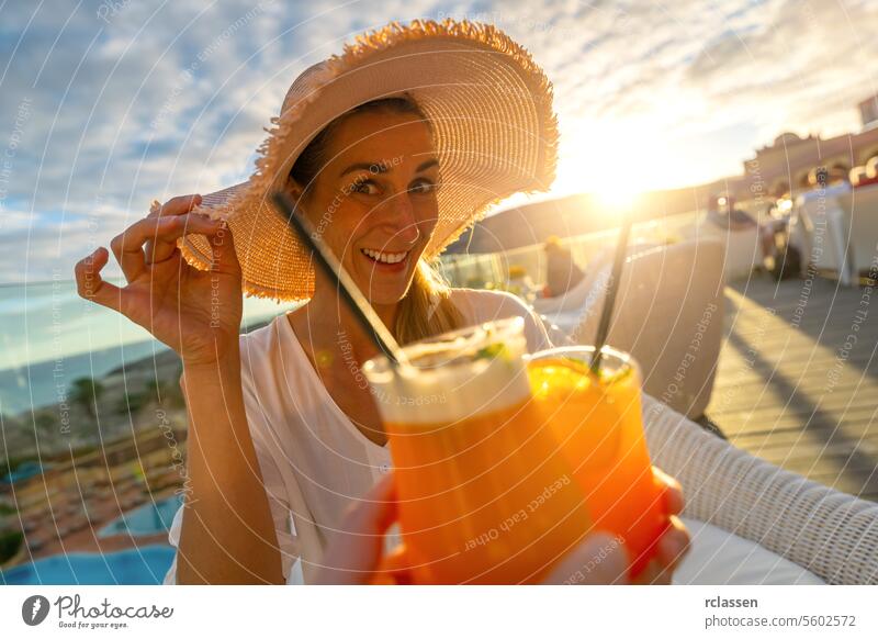 Frau in Sonnenhut lächelnd und Toast mit einem Cocktail am tropischen Strand Hotel auf Sonnenuntergang mit unscharfen Hintergrund Paradiesstrand Playa