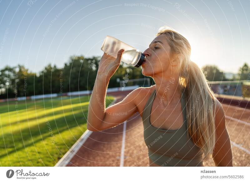 Sportlerin, die auf einem Sportplatz aus einer Wasserflasche trinkt Frau trinken Athlet Fitness Hydratation Leichtathletik Gesundheit Wellness Sportbekleidung