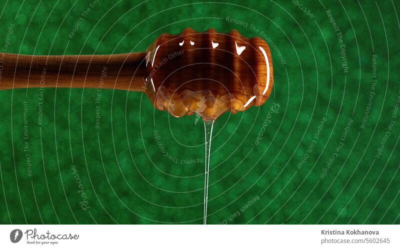 Bio-Honig fließt aus einem hölzernen Schöpflöffel auf grünem Hintergrund. Bienenhaus Nahaufnahme Dessert Abblendschalter Lebensmittel golden Gesundheit Liebling