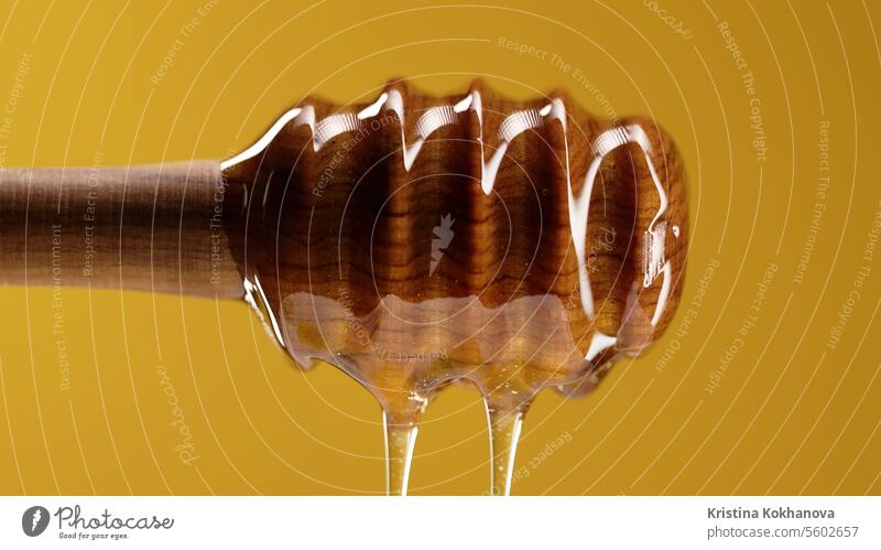 Bio-Honig fließt aus einem hölzernen Schöpflöffel auf einem warmen gelben Hintergrund. Bienenhaus Nahaufnahme Dessert Abblendschalter Lebensmittel golden