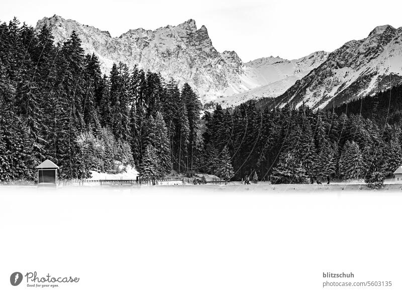 Ein Bergsee mit Nebel und Spaziergänger auf einem Damm. Im Hintergrund spitze Berge und ein Skigebiet Lenzerheide Landschaft Natur Umwelt Schweiz Alpen
