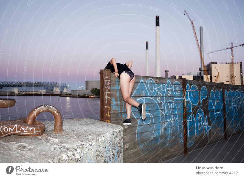 Ein wildes Mädchen erkundet urbane Räume in Kopenhagen, Dänemark. Der Beton-Dschungel ist ein perfekter Ort für ein wunderschönes Dessous-Model. Sie zeigt ihren sexy Rücken, während sie auf eine mit zufälligen Wandmalereien bemalte Mauer klettert. Ein lila Abendhimmel sorgt für romantische Stimmung.