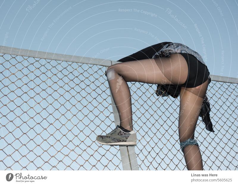 Ein wildes Mädchen klettert heftig über einen Zaun. Ihr sexy schwarzes Höschen und ihre langen Beine sind das Hauptmotiv dieses Bildes. Man hat aber auch das Gefühl, dass hier ein Aufstand im Gange ist.