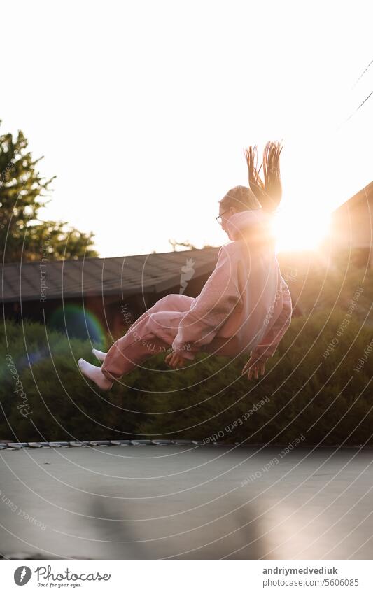 Glückliches kleines Kind Mädchen hat Spaß und springt auf Trampolin im Freien, im Hinterhof des Hauses auf sonnigen Sommertag, aktive Erholung im Sommerurlaub. Glückliche Kindheit Konzept. Tag der Kinder.