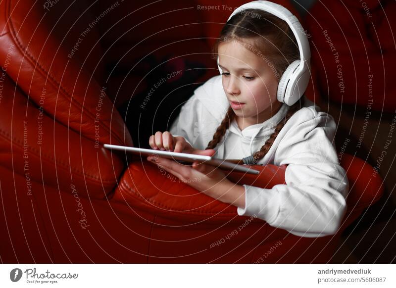 Konzentrierte Teenager-Mädchen in Kopfhörer spielt Spiel, kommunizieren im Internet Social Media, hört Musik oder Online-Studien zu Hause auf digitalen Tablet sitzen auf dem Sofa. Kinder Tech-Sucht Konzept