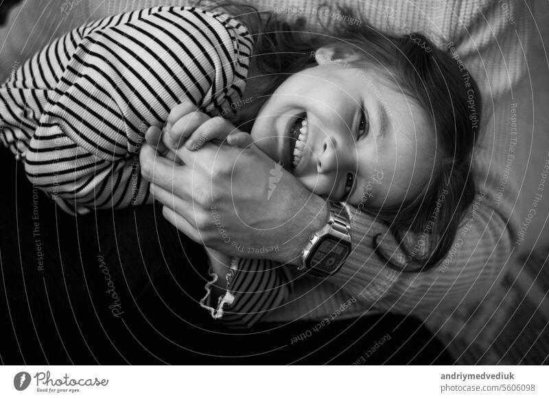 Frohen Kindertag. Schwarz-Weiß-Foto von unerkennbaren Vater mit liebenswerten lachende kleine Tochter haben Spaß verbringen Zeit zusammen am Wochenende zu Hause. Playful Kind Mädchen und Papa umarmen