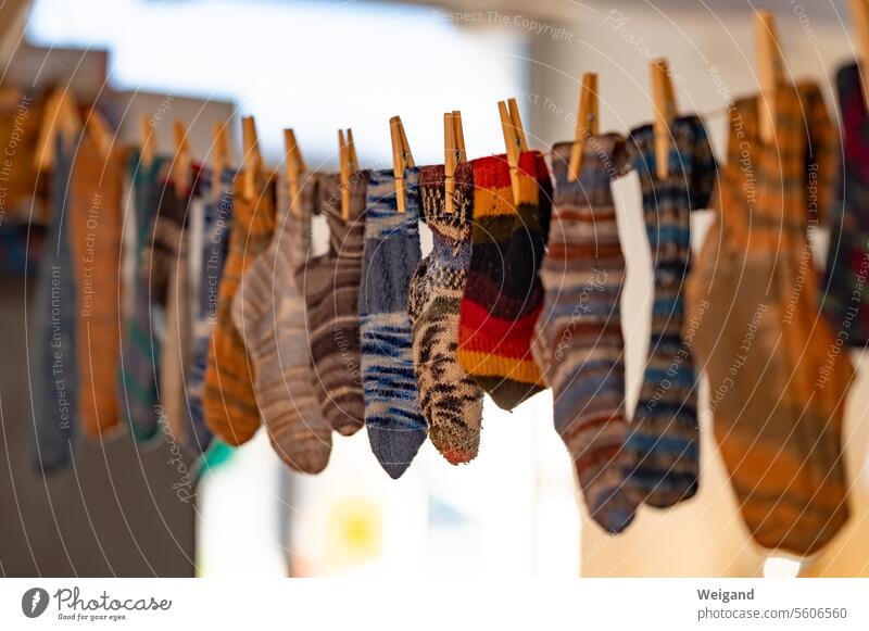 Bunt gemusterte, selbst gestrickte warme Socken in allen Farben, hängen mit Wäscheklammern aus Holz befestigt ordentlich auf einer Wäscheleine nebeneinander