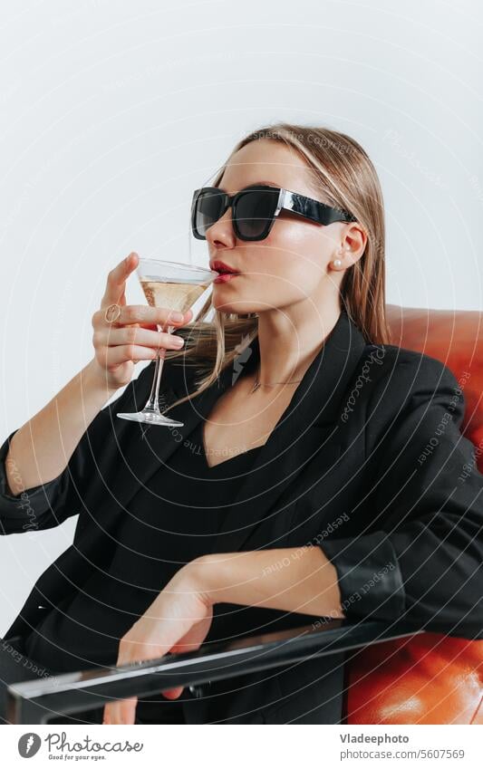 Lady Boss in total schwarzem Look sitzt im Sessel und trinkt Wein, Wochenende jung Frau Martini Mode Armsessel Stil Anzug Jacke unabhängig Chef Model trinken