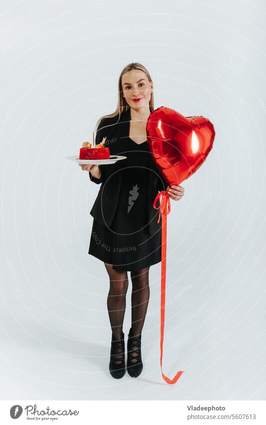 Junge Frau in schwarzer Jacke und Rock hält Herzform Ballon und Kuchen auf weißem Hintergrund feiern schön Luftballon rot Liebe jung Symbol Anzug Büro