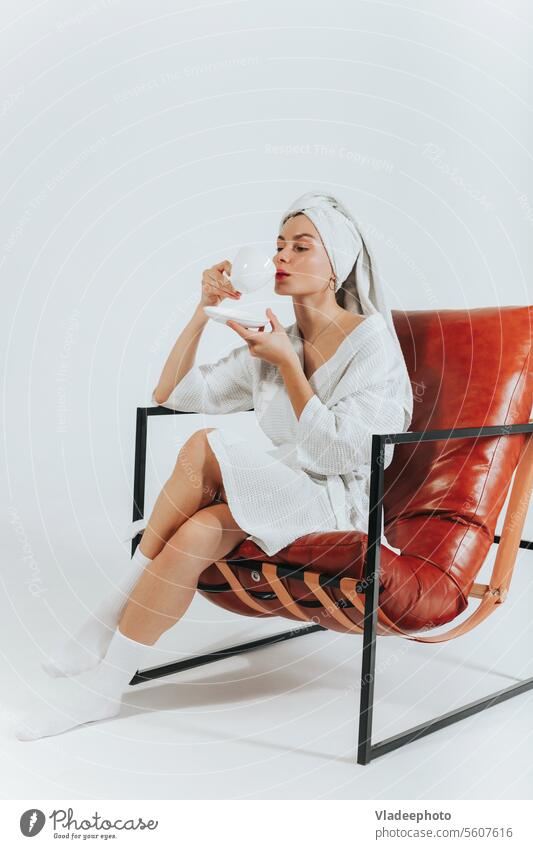 Frau im Bademantel, Kaffee oder Tee trinkend, mit einem weißen Handtuch um den Kopf gewickelt. Weißer Hintergrund Decke Morgen heimwärts Lifestyle Streu Mädchen