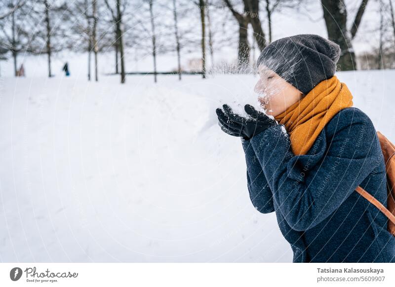 Eine Frau bläst Schnee, den sie in ihrer Handfläche gesammelt hat, vor dem Hintergrund der verschneiten Natur Winter kalt Fröhlichkeit Glück Freude Menschen