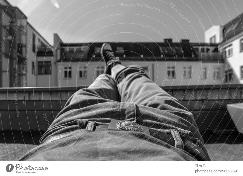Mann ruht mit ausgestreckten Beinen auf dem Dach aus Chucks s/w Prenzlauer Berg chillen Hof Berlin Sonnenlicht Stadt Stadtzentrum Schwarzweißfoto Hauptstadt Tag