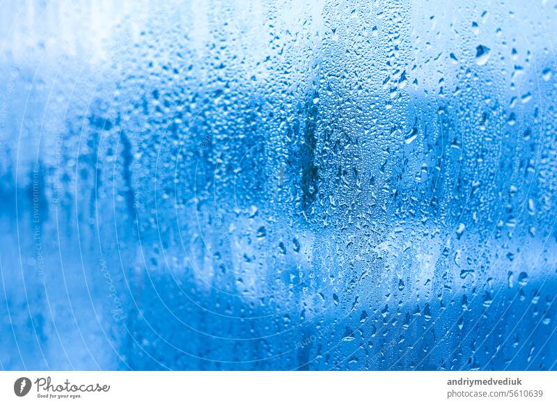 Blauer Hintergrund von Glas von Metall-Kunststoff-Fenster mit Wassertröpfchen Kondensation drinnen Raum. Hohe Luftfeuchtigkeit. Feuchtigkeitskondensation Probleme, heißer Wasserdampf kondensiert auf Fenster in der kalten Jahreszeit.