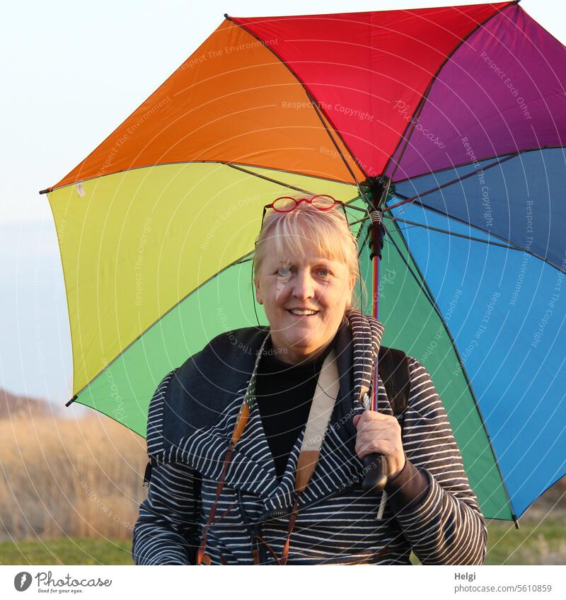 fröhliche Seniorin mit buntem Schirm Mensch Frau Erwachsene Porträt Oberkörper Gesicht Blick in die Kamera Regenschirm Jacke Streifen Frühling Lächeln blond