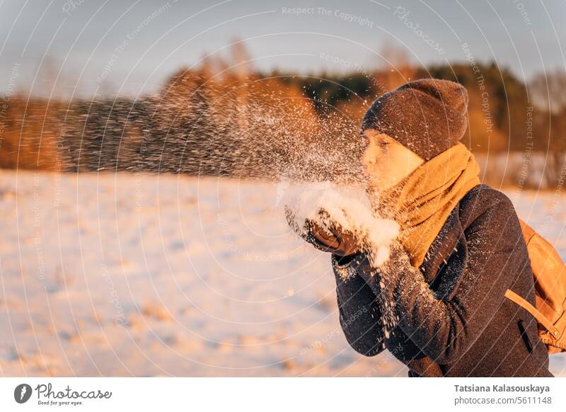 Eine Frau bläst abends bei Sonnenuntergang eine Handvoll Schnee aus ihren Händen Winter Schlag Abend Menschen Person Europäer weiß Erwachsener
