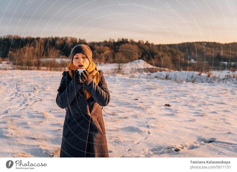 Eine Frau im Winter mit einer Handvoll Schnee in ihren Händen, bereit, ihn wegzupusten warme Kleidung Schlag Handfläche Menschen Person Europäer weiß