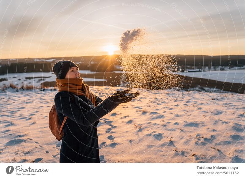 Eine Frau auf einem schneebedeckten Feld wirft mit ihren Händen Schnee vor dem Hintergrund eines Sonnenuntergangs werfen Hand Sonnenuntergang. Winter