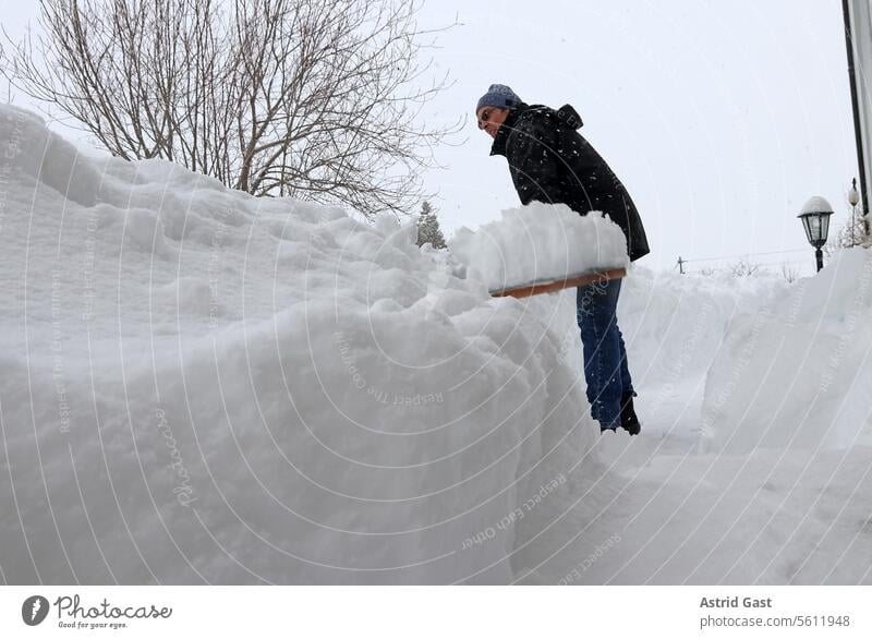 Ein Mann räumt hohen Schnee auf einem Fußweg vor einem Haus weg schneeräumen mann schneien winter räumdienst schneeschaufeln winterdienst eingeschneit straße