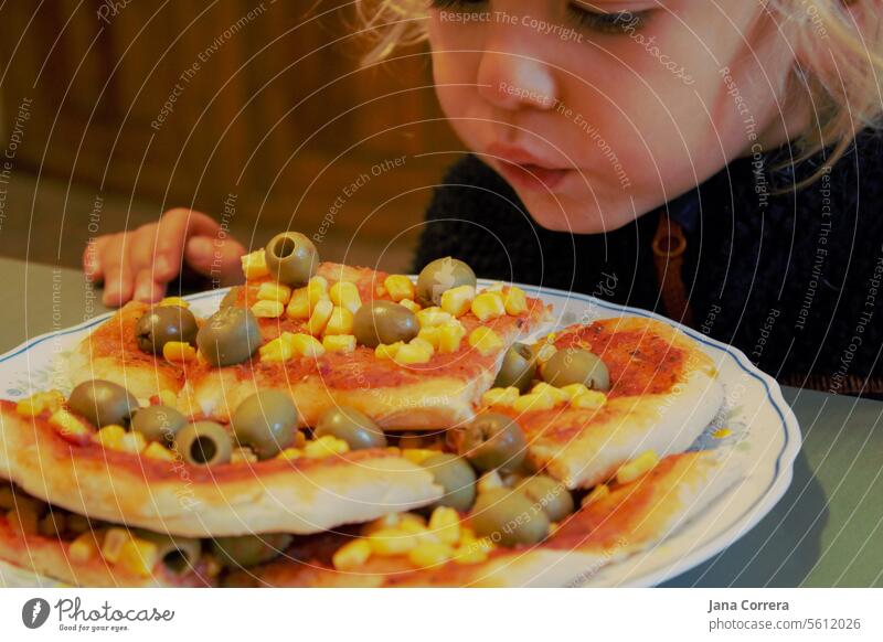 Ein Kind pustet auf frisch gebackene Pizza Pizza essen vegetarisch vegan Abendessen selbstgemacht belegte Oliven Mais Pizzabrot Pizzateig hungrig pusten heiß