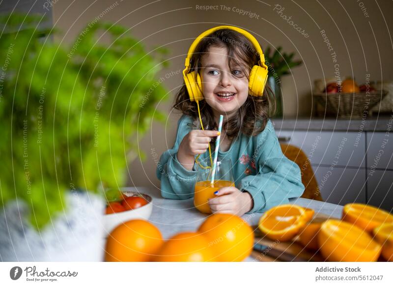 Kaukasisches Kind trinkt zu Hause Saft Mädchen Lächeln Glas Wegsehen hören Musik Technik & Technologie Kopfhörer Stroh heimwärts Selektiver Fokus Lifestyle